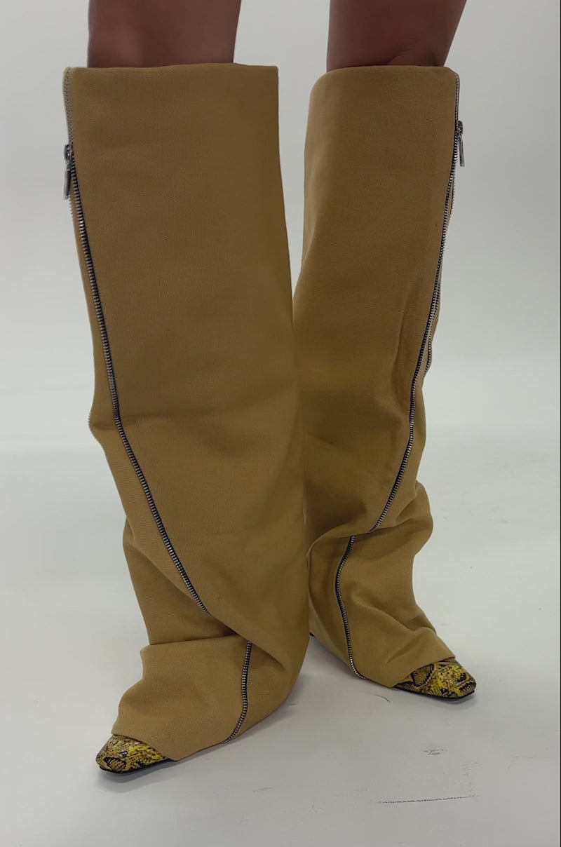 Video of woman modeling AKIRA GOLD RASHAWN KHAKI AND SNAKE BOOT—oversized, slouchy over-the-knee boots featuring visible diagonal zippers and pointed tips that partly reveal yellow and black details.