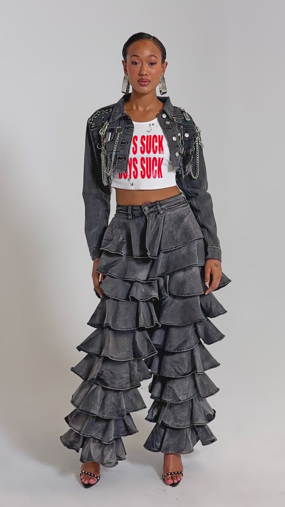 A video of a woman in the LOOK THIS WAY RUFFLE DENIM PANT, paired with a cropped graphic tee, a fringed studded denim jacket, and high heels.