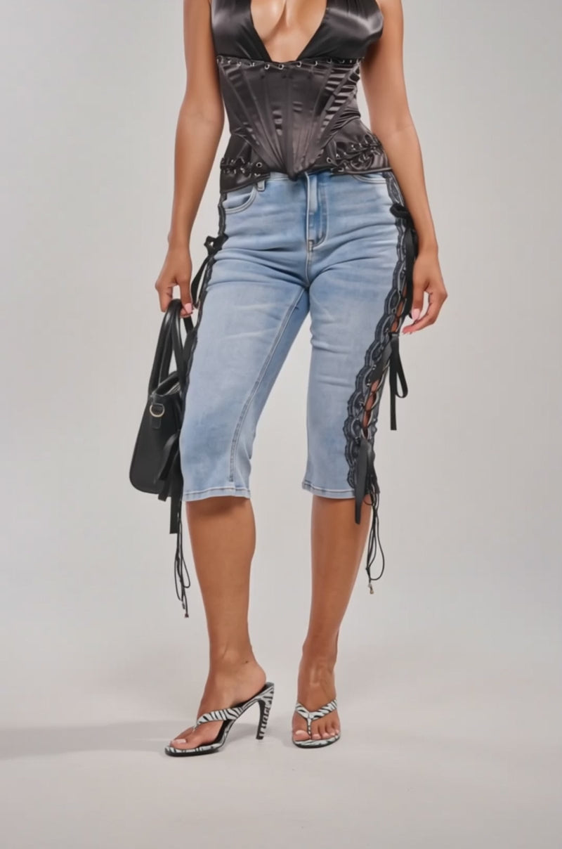 Video of woman modeling the LOTS OF LOVE TO GIVE DENIM CAPRI WITH LACE, a black halter top, hoop earrings, heeled shoes, and holds a small black handbag.