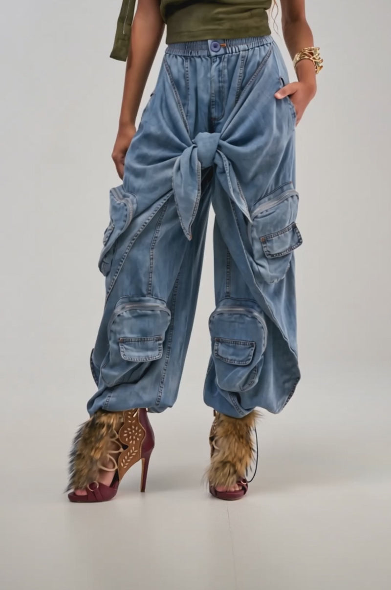 Video of a woman modeling the DO THE MOST TIE FRONT PANT IN DENIM, which features a wide leg cargo design with multiple pockets and a front tie detail.
