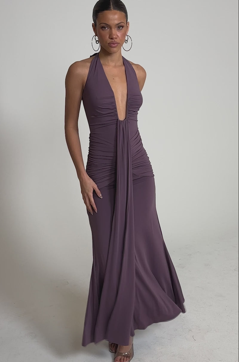 A video of a woman wearing the ISLAND LOVE MAXI DRESS in mauve, featuring a sleeveless halter neck, deep V-neckline, ruched bodice, and flowing skirt. 