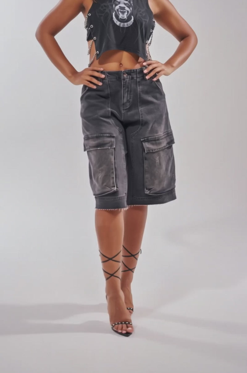 A video of a woman poses in the GOT THAT DOG IN ME EMBELLISHED TANK—styled with long black cargo shorts and strappy heels.
