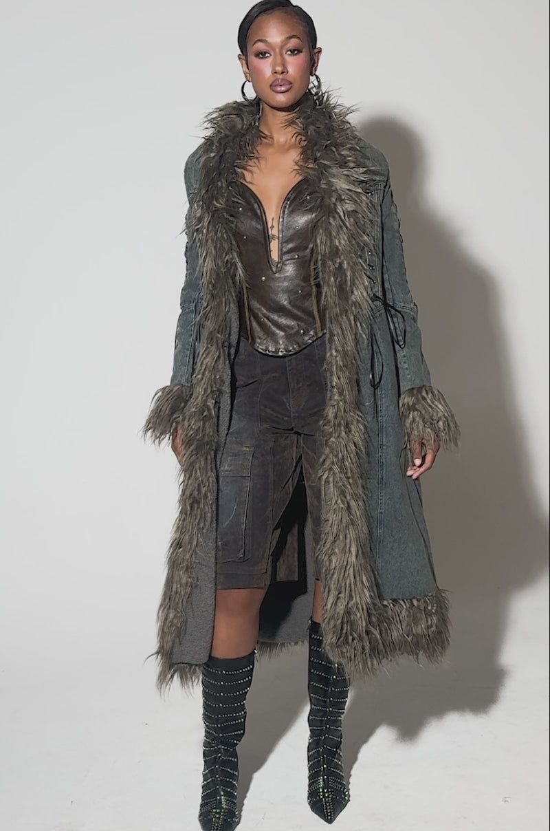 Video of woman modeling the SADE FUR TRIM DENIM TRENCH, featuring thick faux fur on the collar, cuffs, and hem. She pairs it with hoop earrings and a sleek hairstyle, posing against a light background.