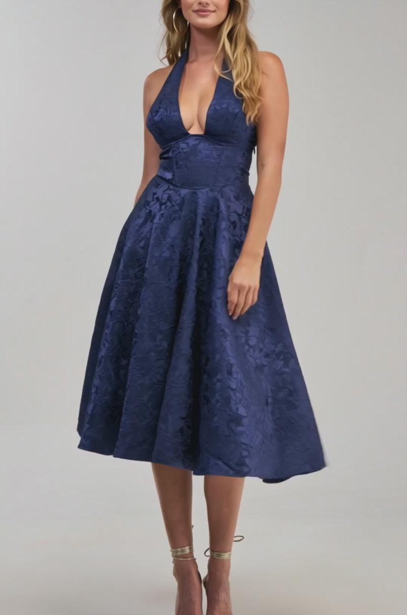 Video of a woman modeling the SWEET CAROLINE HALTER MIDI DRESS IN NAVY—a sleeveless, halter-neck, knee-length cocktail party dress with a flared skirt and subtle floral texture.