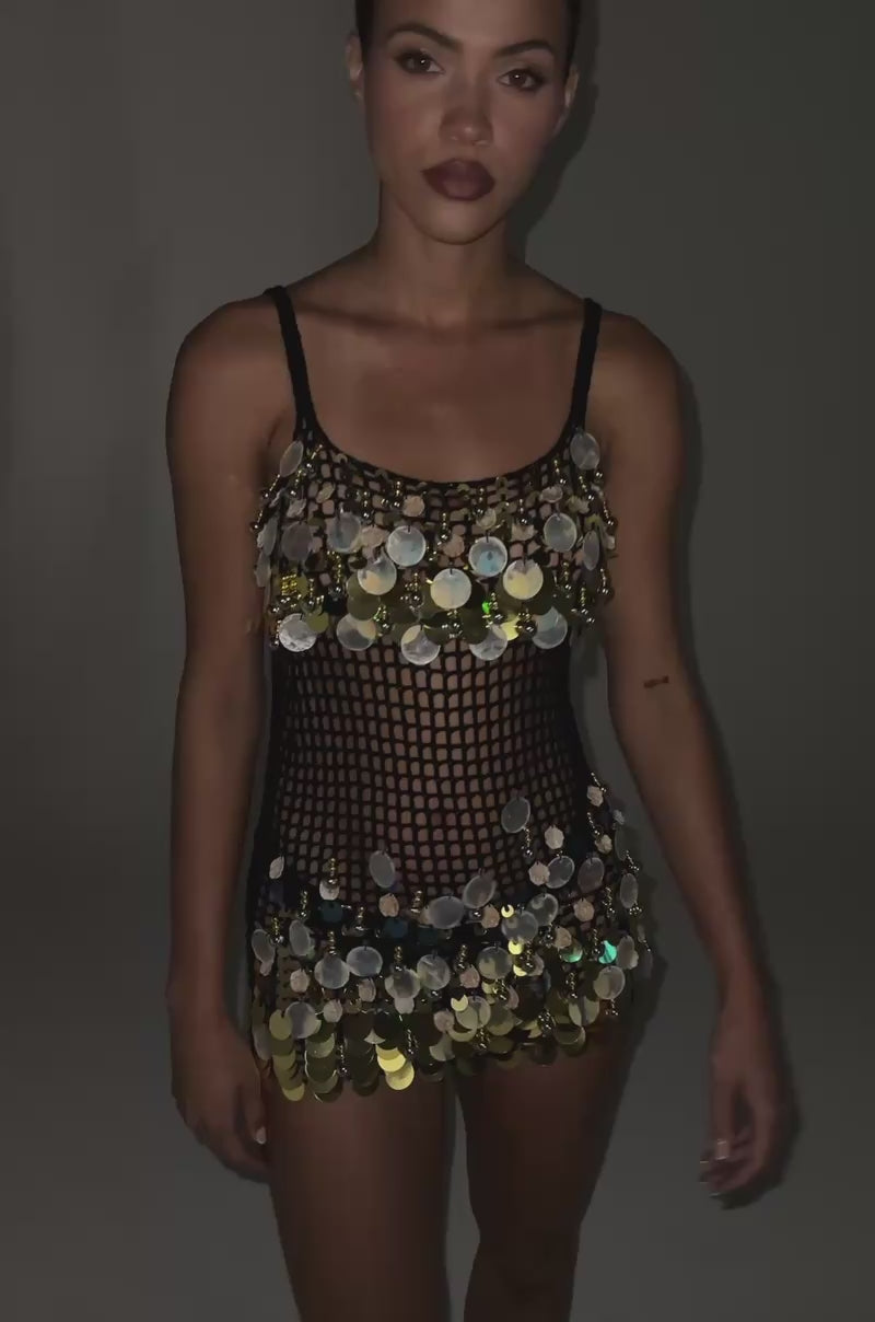 Video of woman modeling the RESORT LIVING SEQUIN CROCHET MINI DRESS—a sleeveless black mini dress embellished with bold gold and silver sequins.