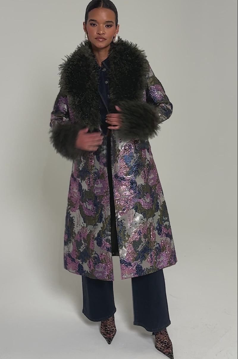 Video of woman modeling the GEORGINA BROCADE TRENCH, a long coat with floral metallic brocade and luxe faux fur trim on the collar and cuffs, a woman stands confidently against a plain background.