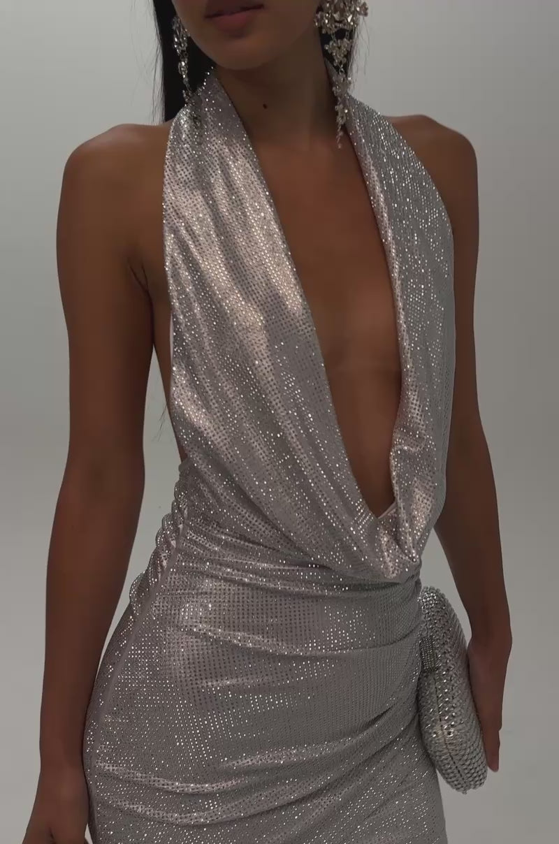 Video of a woman modeling the DONT PLAY WITH ME RHINESTONE MINI DRESS IN SILVER, featuring a shimmering rhinestone design and a deep cowl-neck halter neckline.