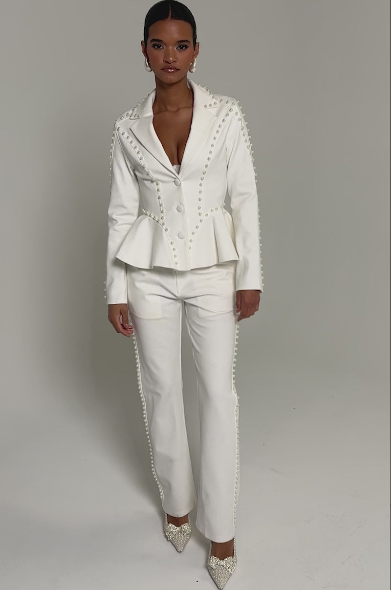 Video of woman modeling the CHLOE PEARL TROUSER, which features high-rise cotton fabric and decorative side buttons, paired with white embellished shoes, a person stands against a plain light background.