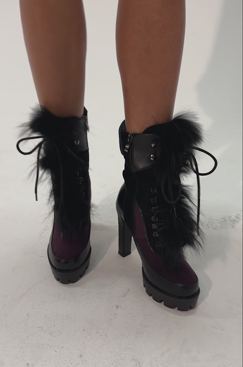 Video of a woman modeling the AKIRA GOLD SNUG PURPLE MULTI FUR COMBAT BLOCK HEEL BOOTIE, featuring high-heeled, lace-up streetwear design with chunky soles, black fur trim, and a bold mix of black, dark green, and burgundy panels.