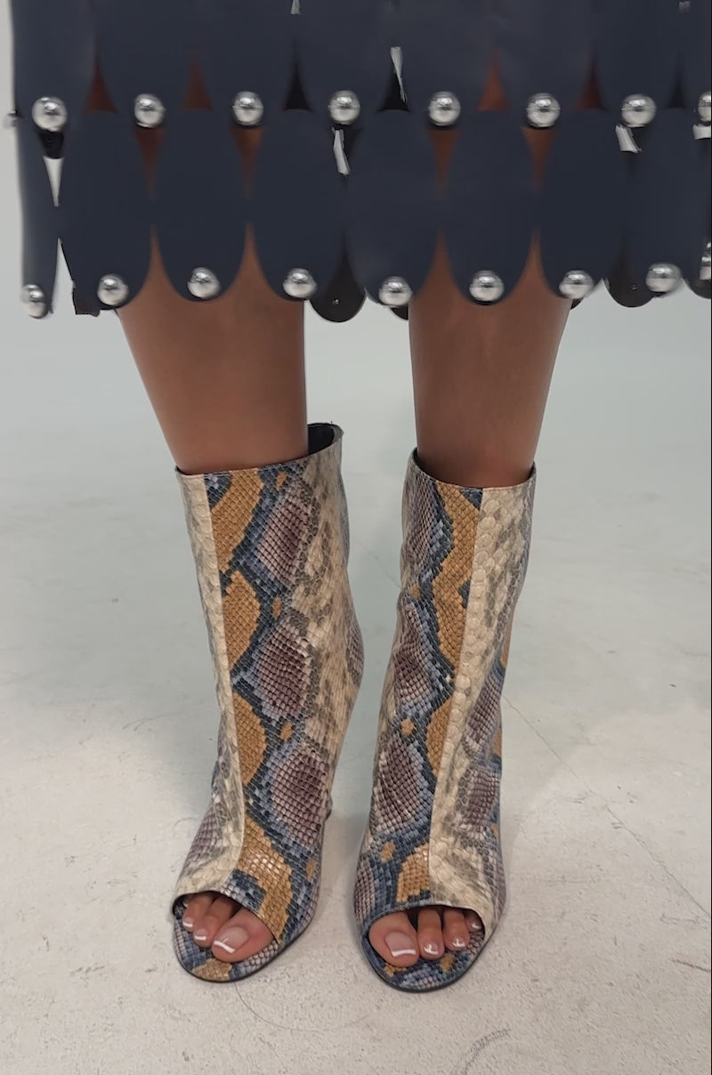 A video of a model wearing the AZALEA WANG FAOI SNAKE MULTI OPEN TOE WEDGE BOOTIE which features a chic snake print in beige, yellow, blue, and brown with a sculptural inverted wedge heel and an open toe design.