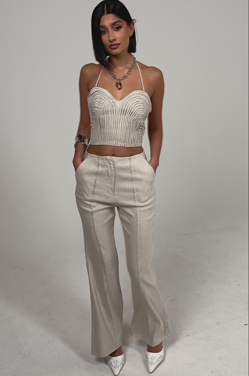 A video of a woman wearing the LAY IT LOW TROUSER, high-rise wide-leg linen pants in beige, paired with a matching sleeveless halter crop top. 