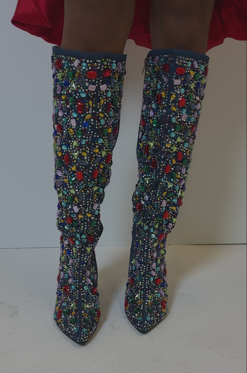 Video of person showing off the AZALEA WANG EMBER RHINESTONE MULTI STILETTO BOOT. The boot features a knee-high length and is embellished with an intricate pattern of colorful gemstones in shades of red, purple, turquoise, and yellow.