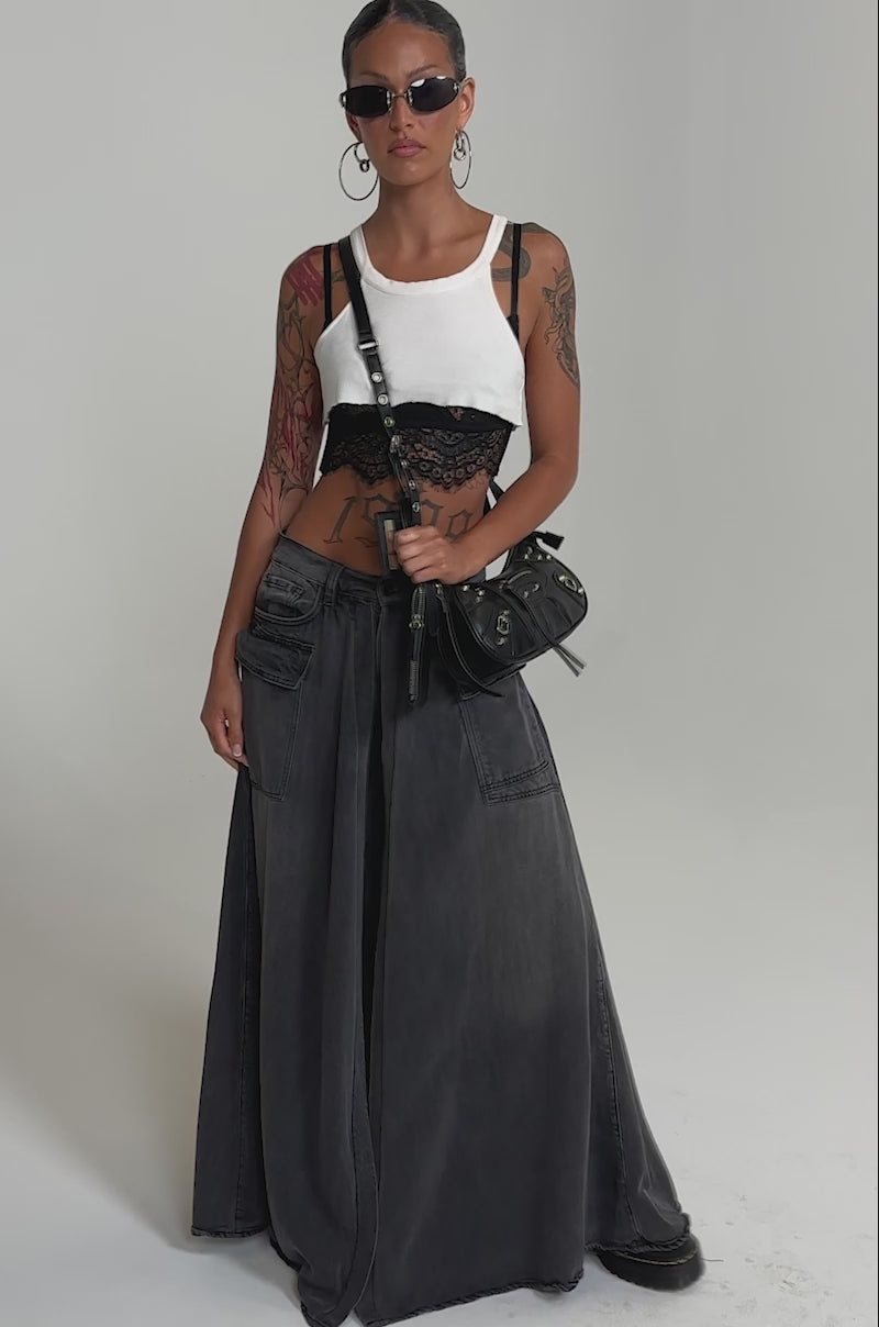 A video of a woman wearing the MIXED EMOTIONS DENIM PANT, styled with straight-leg pockets, a white crop top over a black lace bralette, sunglasses, large hoop earrings, and a black crossbody handbag.