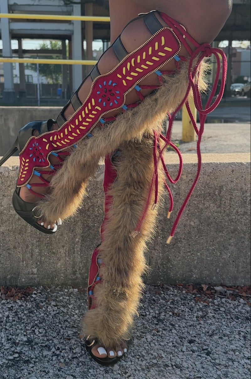 A video of a person wearing textured black shorts and AZALEA WANG SHAINE BLACK MULTI GLADIATOR STITCH AND FUR SANDALS with striking red, blue, and yellow details stands on a city sidewalk near a crosswalk.