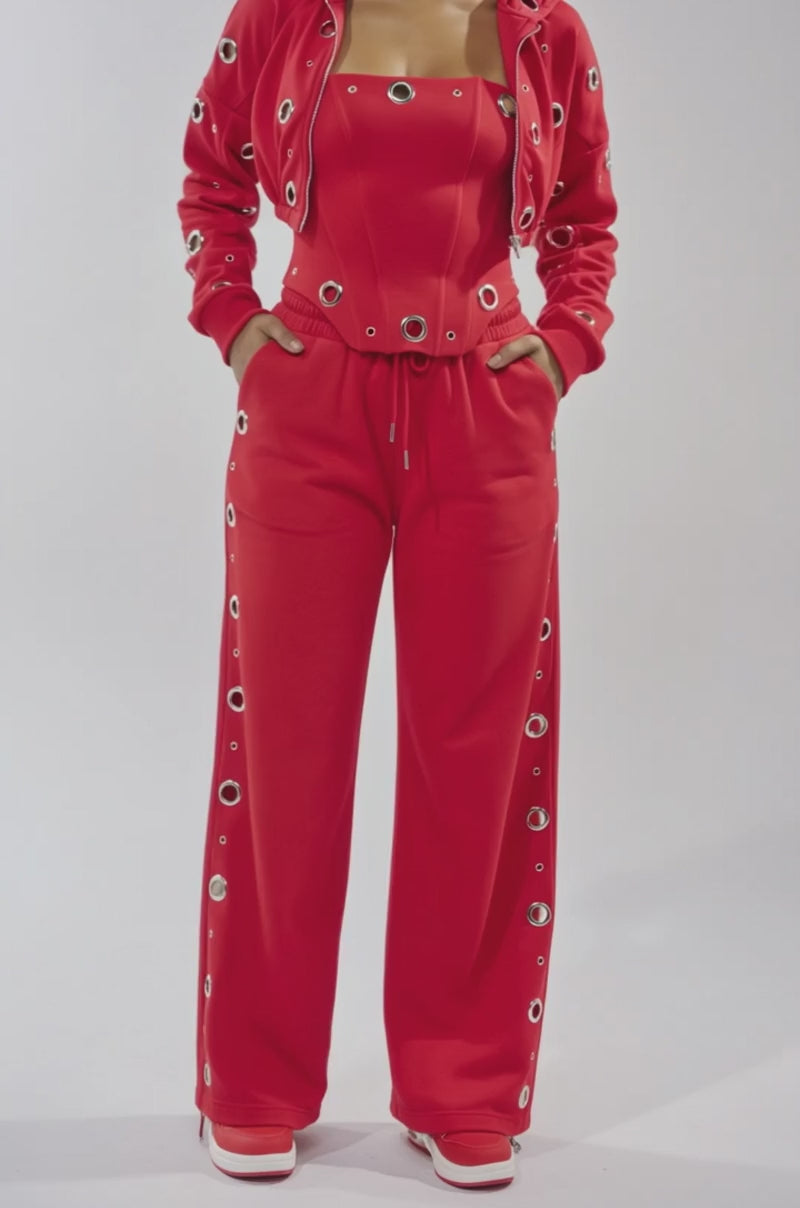 A video of a woman wearing the COMFY COZY CORSET in vibrant red cotton, styled with wide-leg pants and a matching jacket embellished with metallic grommets. 