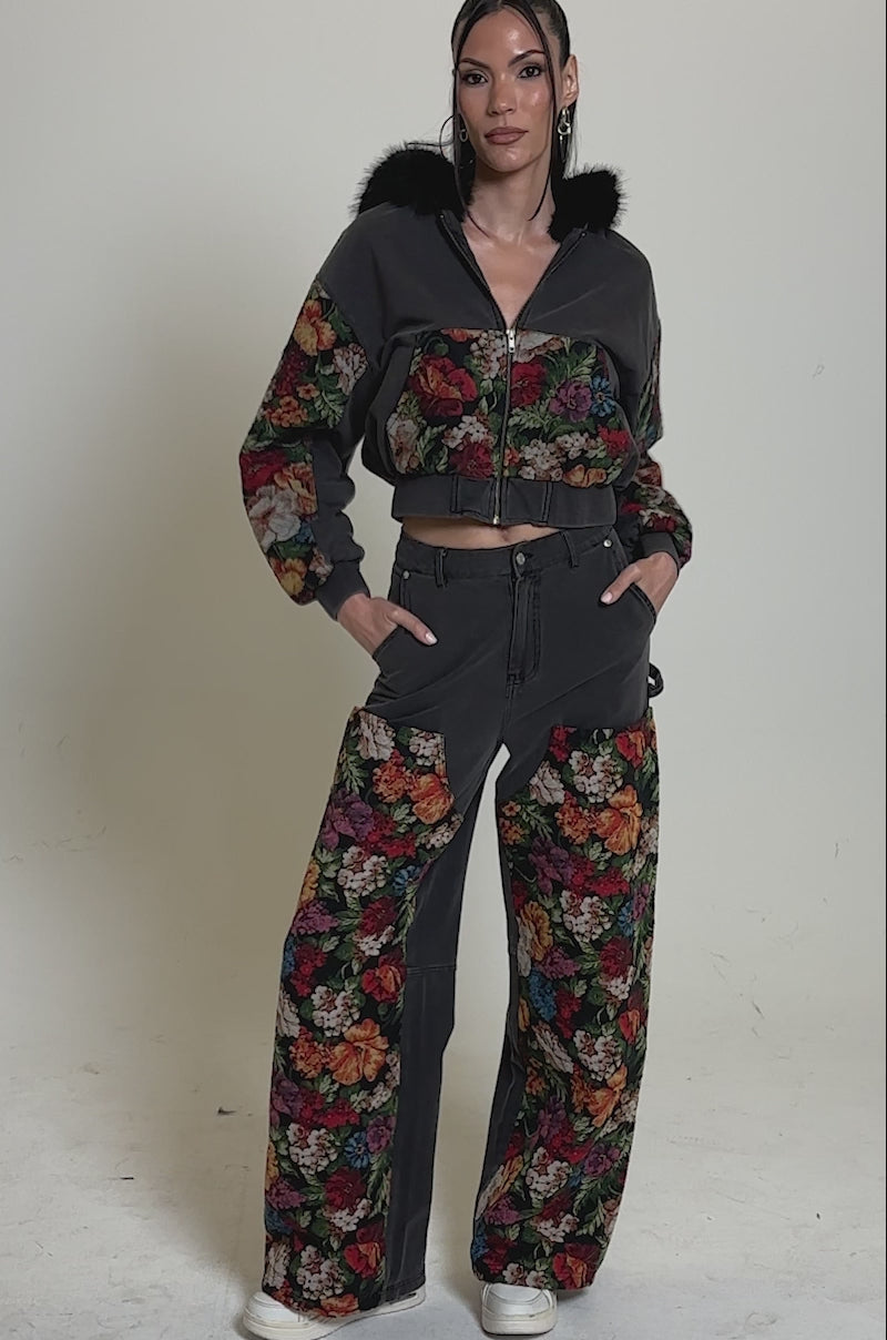 Video of woman modeling the TRY ME FLORAL DENIM ZIP UP SWEATSHIRT with a black faux fur-trimmed hood and colorful floral patterns, paired with matching high-waisted pants, stands against a plain light background.