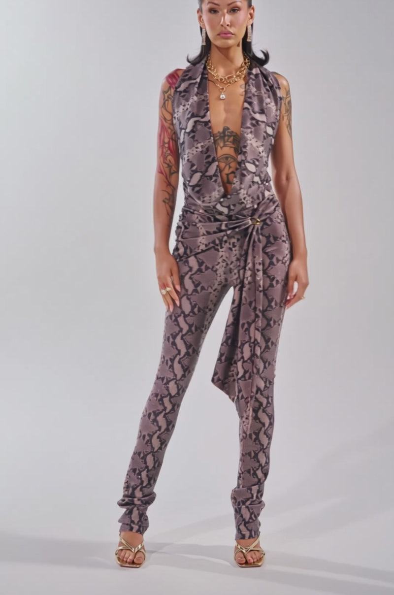 Video of woman modeling the VENOM KISS RHINESTONE LEGGING—high-waisted, brown snake-print flare leggings with a matching sash and gold open-toe heels, set against a plain background.