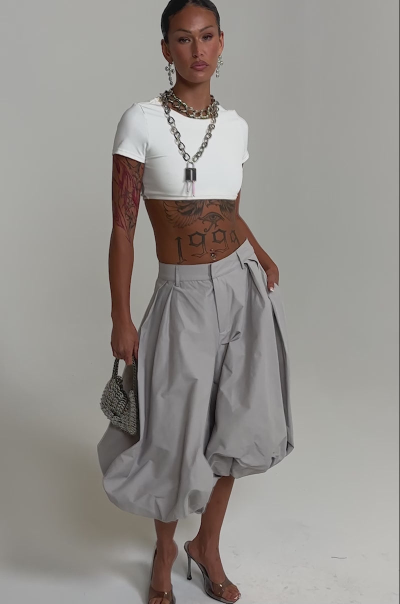 A video of a model wearing the GLOW GAUCHO PANT in grey with a white crop top and heeled sandals. 