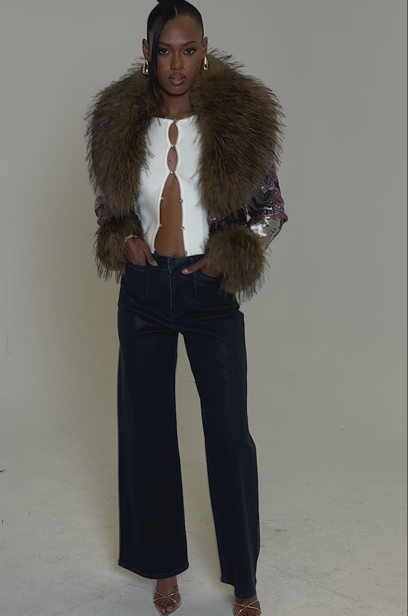 Video of woman modeling the  GISELE FUR TRIM MOTO IN BROCADE jacket featuring a bold faux fur collar, paired with dark high-waisted pants, hoop earrings, and a high bun against a plain background.