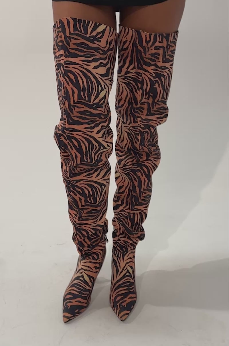 Video of a woman modeling the AZALEA WANG STEPHAN TIGER THIGH HIGH BOOT—vivid orange with black tiger stripes, a pointed toe, a side zipper, and stiletto heels.