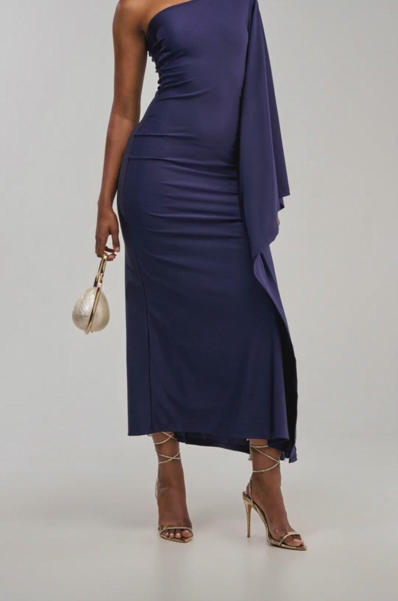 Video of a woman modeling the MAEVE ONE SHOULDER MAXI DRESS IN DEEP NAVY, a fitted design featuring a draped sleeve.