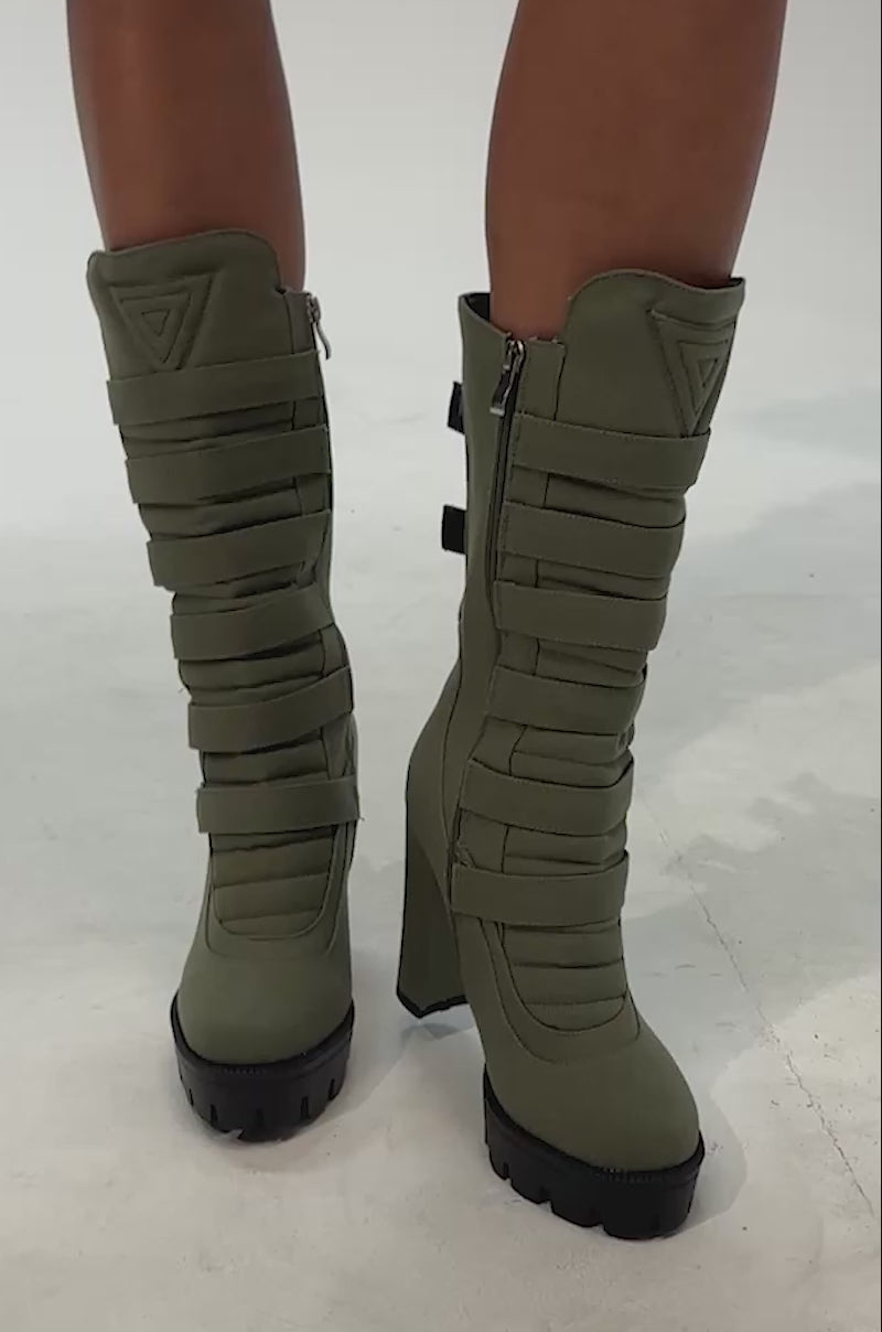 Video of woman modeling the AZALEA WANG VIOREN OLIVE CANVAS BLOCK BOOTIE—a pair of olive green high-heeled boots featuring thick black soles and layered strap detailing. 