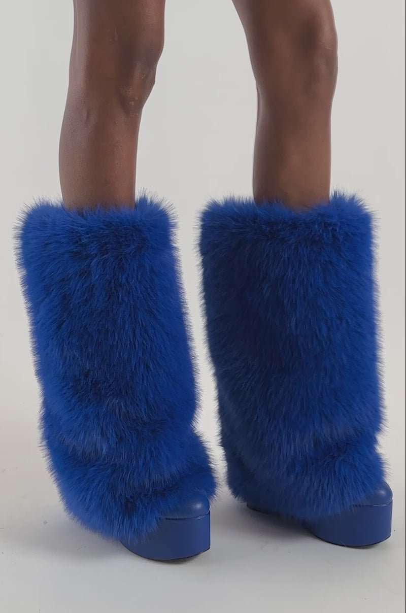 Video of a woman modeling the AKIRA GOLD SALVIENNE BLUE FUR FLATFORM BOOT, a tall wedge boot featuring a vibrant cobalt blue color and furry texture. 