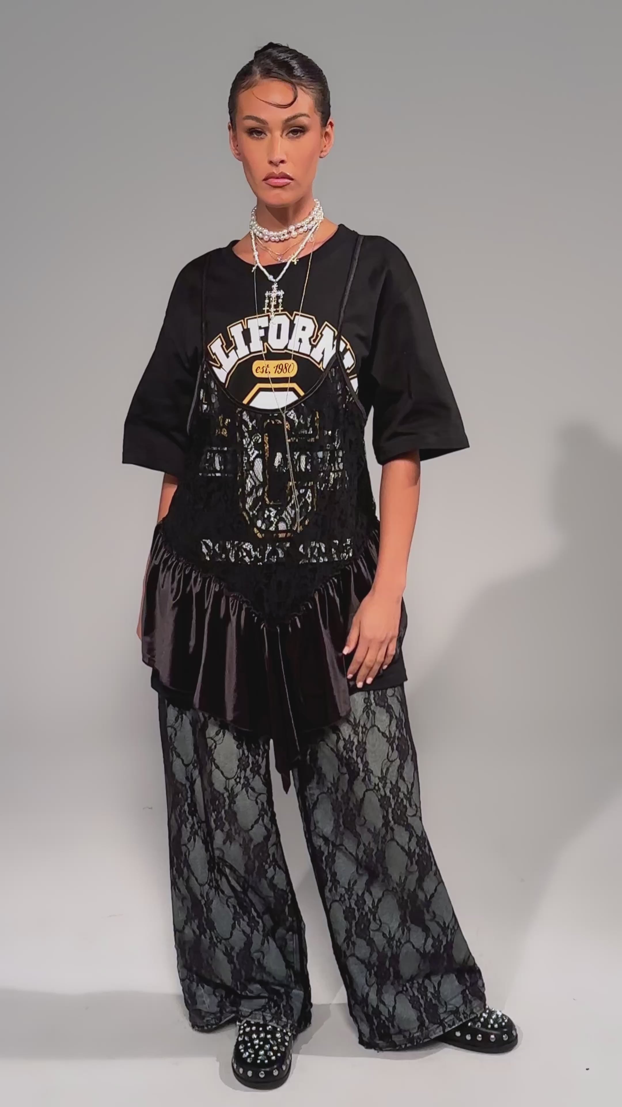 Video of woman modeling the BEVERLY HILLS DIVA LACE OVERLAY TEE, layered with a black lace and satin dress, dark lace pants, and multiple necklaces.