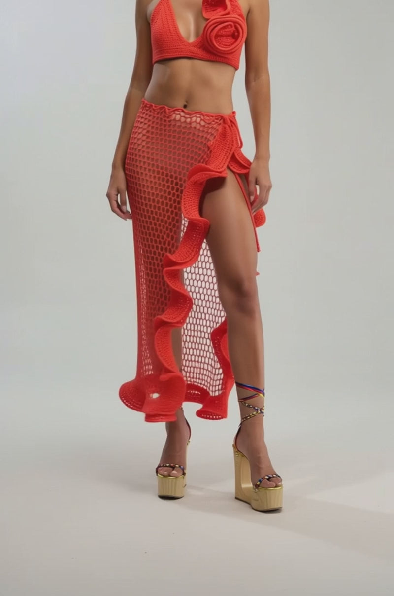 A video of a person wearing the BEACH BABE CROCHET MAXI SKIRT, a bright red ruffle maxi with a high slit, styled with colorful wrap-around platform sandals against a plain background.