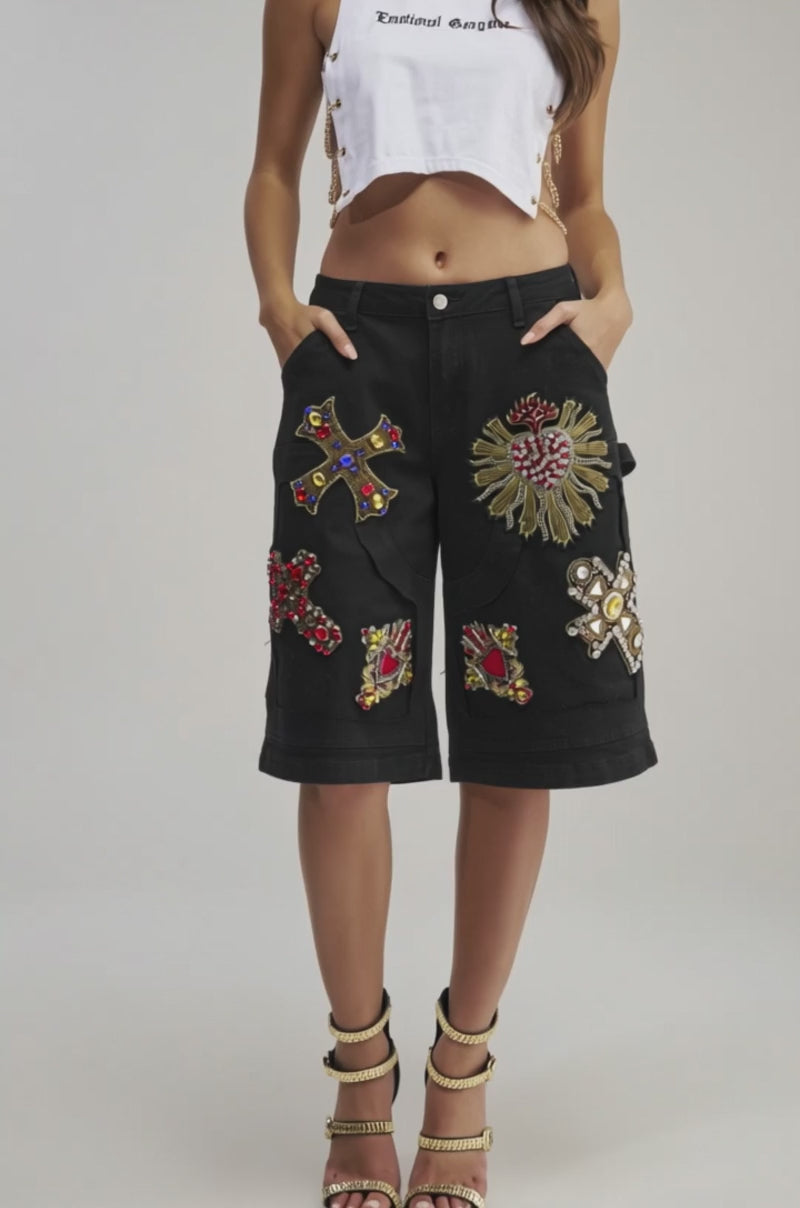 A video of a person wearing WILD AND FREE DENIM SHORTS, featuring ornate, colorful embroidered patches, paired with black high-heel sandals with gold chain straps. 