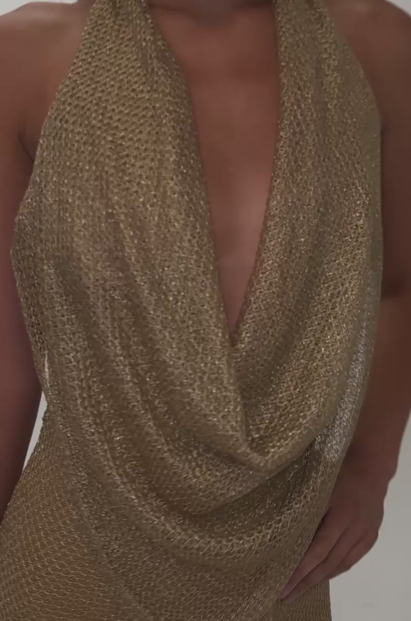 Video of a woman modeling the ELECTRIC GLOW WOVEN MINI DRESS—featuring a gold knit halter design with a textured, draped neckline.