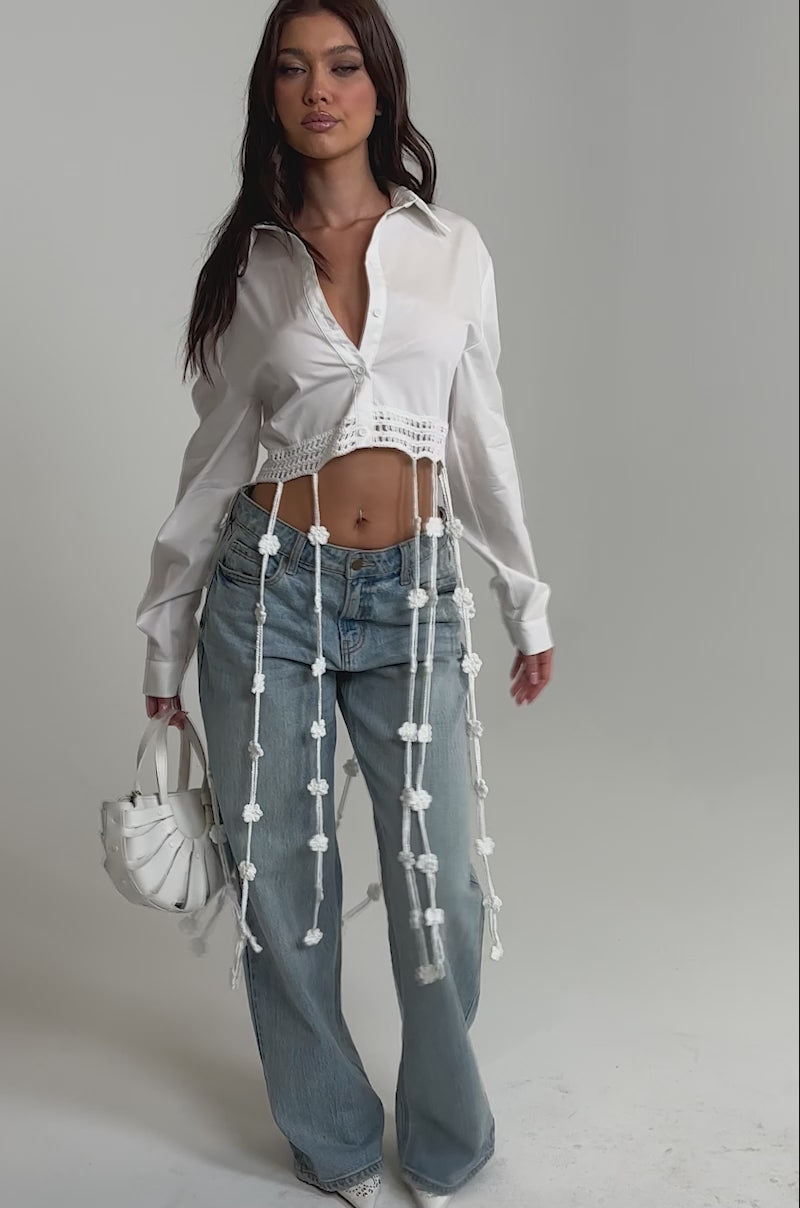 Video of woman modeling the PETAL DRIFT CROCHET DETAIL BLOUSE, light blue wide-leg jeans, white pointed shoes, and holding a small white handbag against a plain light background.