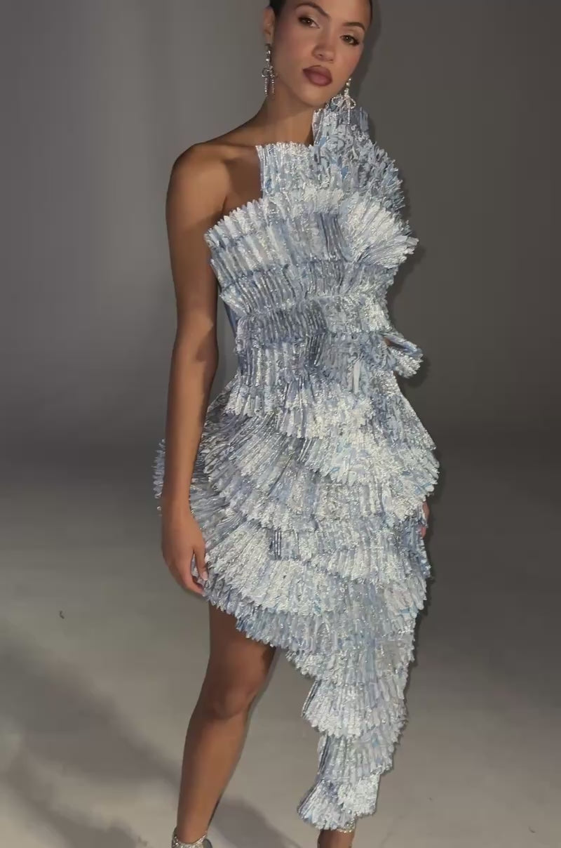 Video of woman modeling the LUST FOR LIFE Asymmetrical Brocade Midi Dress in Blue, featuring sculptural ruffles, fan-like textures, a one-shoulder neckline, and strappy heels against a plain light background.