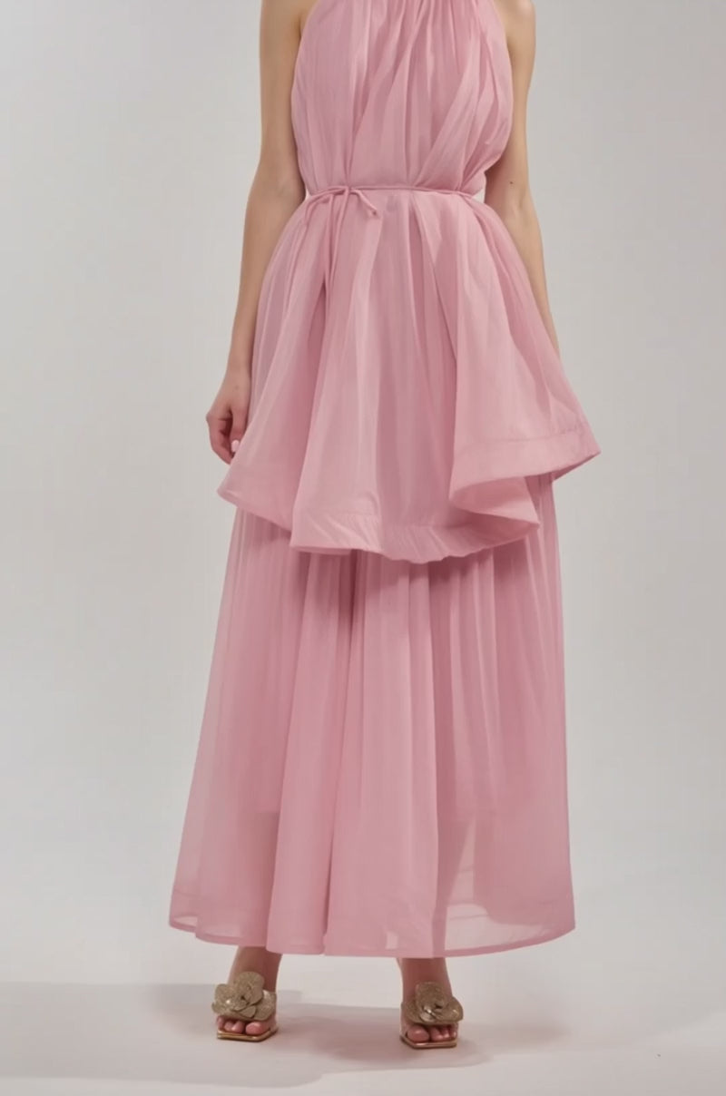 Video of woman modeling the BREEZY GIRL TIERED MAXI DRESS IN BLUSH, a sleeveless blush pink maxi with a billowy layered top, tiered ruffle details, and a wide skirt. She pairs it with beige sandals against a plain light gray background.