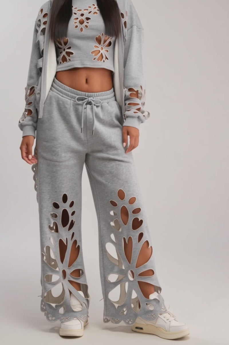 A video of a woman in the GIRLY POP CUTOUT ZIP UP SWEATSHIRT in heathered grey with matching loungewear pants, both featuring large cutout patterns. 