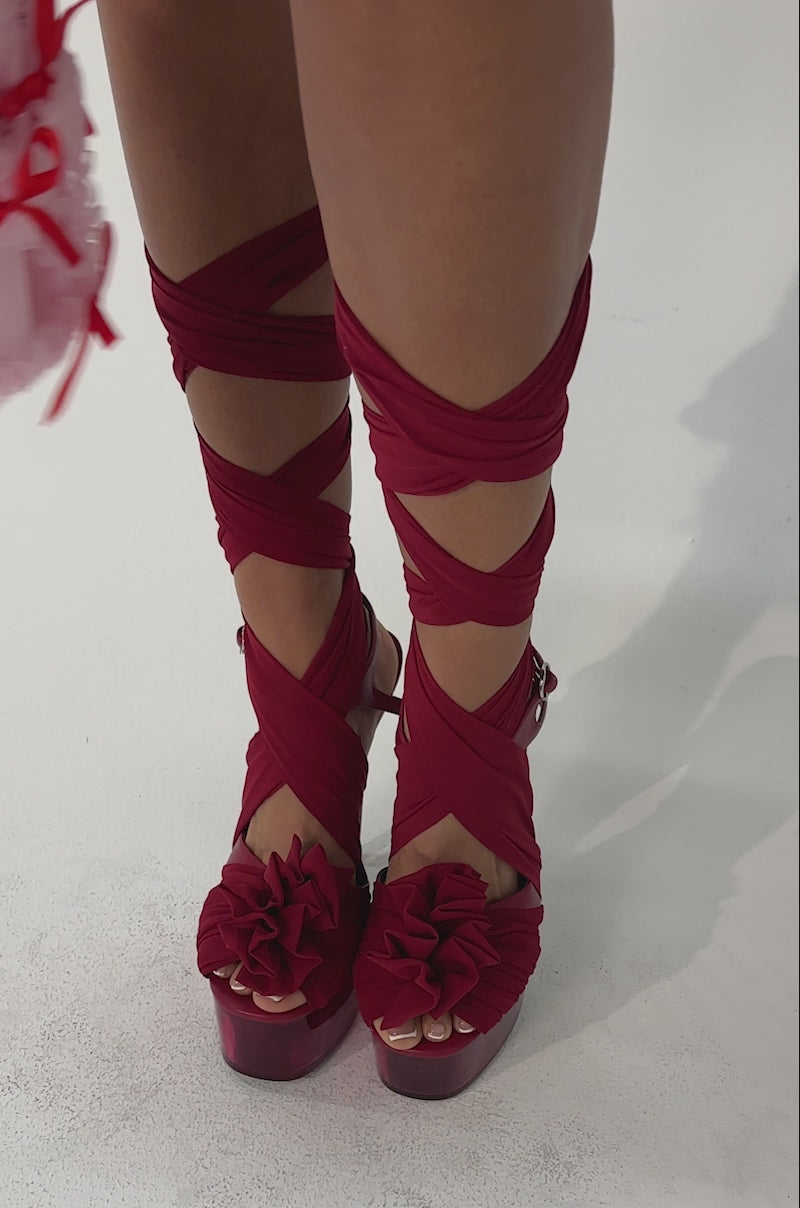 Video of woman modeling the AKIRA GOLD BEAUDEN RED PLATFORM TIE SANDALS, holding a pink frilly handbag with red bows against a plain light background.