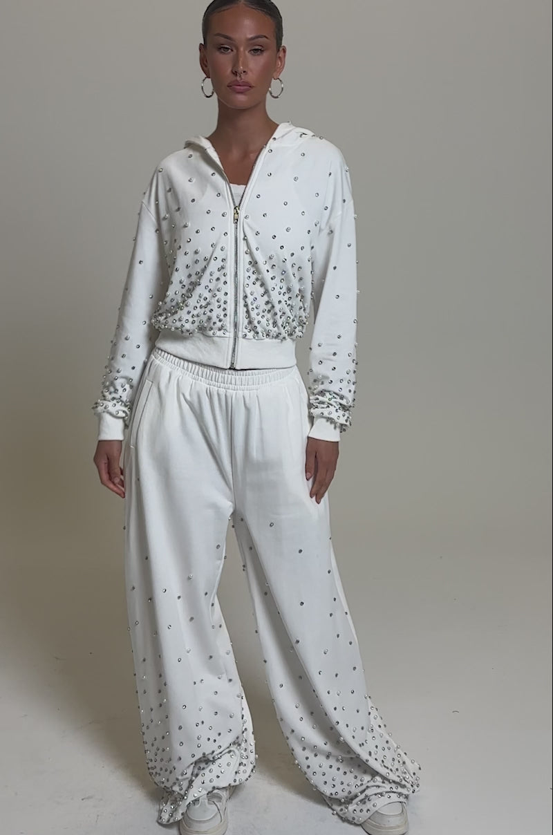 Video of woman modeling the ALL IN WHITE RHINESTONE WIDE LEG JOGGER, paired with a matching cropped hoodie and white shoes.