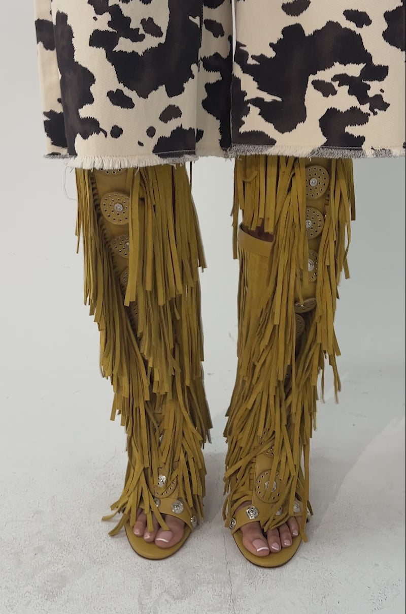 A video of a person wearing knee-length, black and white cow-print shorts and AZALEA WANG SAMEYANA mustard fringe and metal stiletto gladiator sandals. 