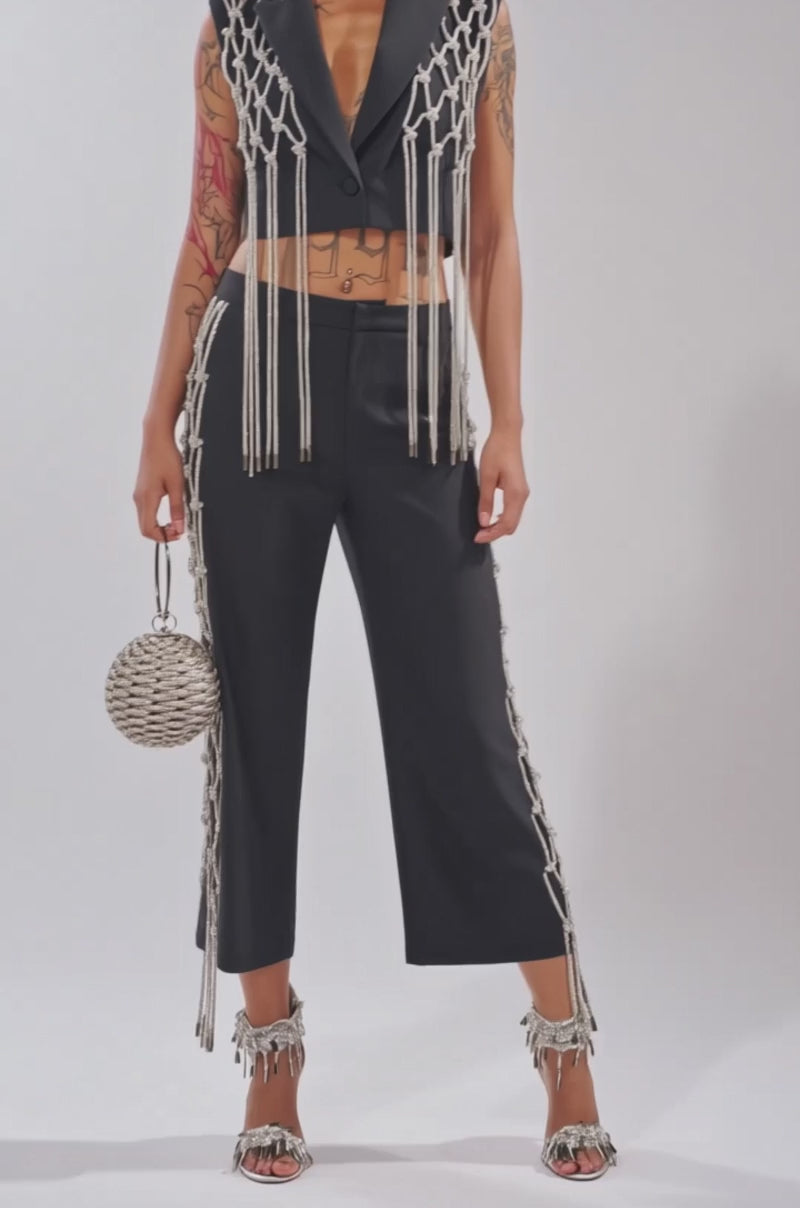 Video of woman modeling the NINA RHINESTONE BLAZER VEST, a sleeveless black cropped blazer featuring knotted silver chains, posing confidently against a light background—perfect for making a statement.