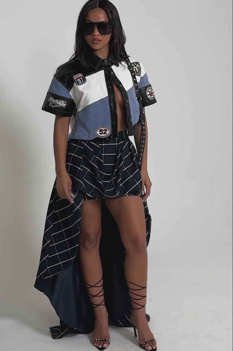 Video of woman modeling the GUESS WHAT STRIPE SHORT SLEEVE BUTTON DOWN with large sunglasses and a navy blue skirt featuring white grid lines