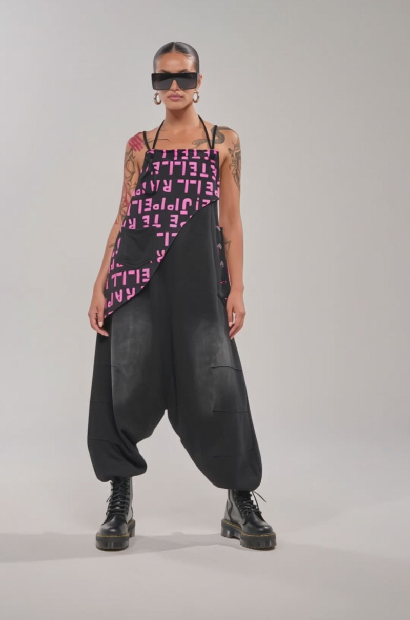 A video of a person wearing the WITH EASE GRAPHIC JUMPSUIT IN BLACK, chunky black boots, large hoop earrings, and sunglasses.