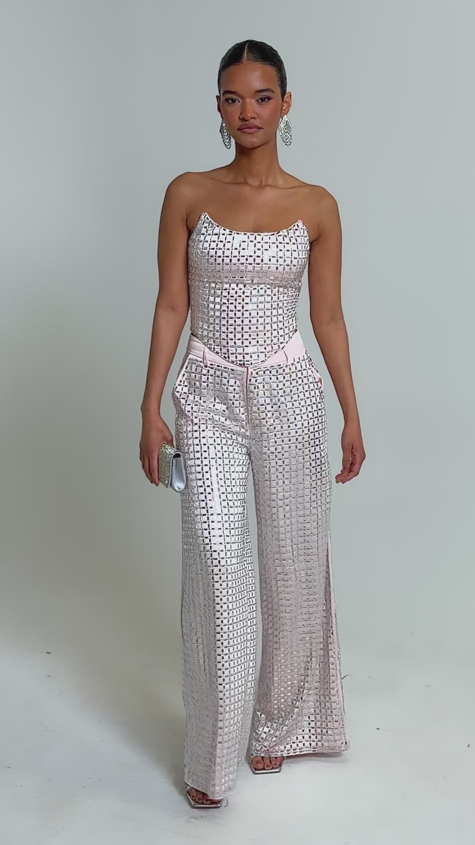 Video of woman modeling the LILA EMBELLISHED SATIN CORSET IN LIGHT PINK and matching pants, accessorized with hoop earrings as she poses confidently against a plain background.