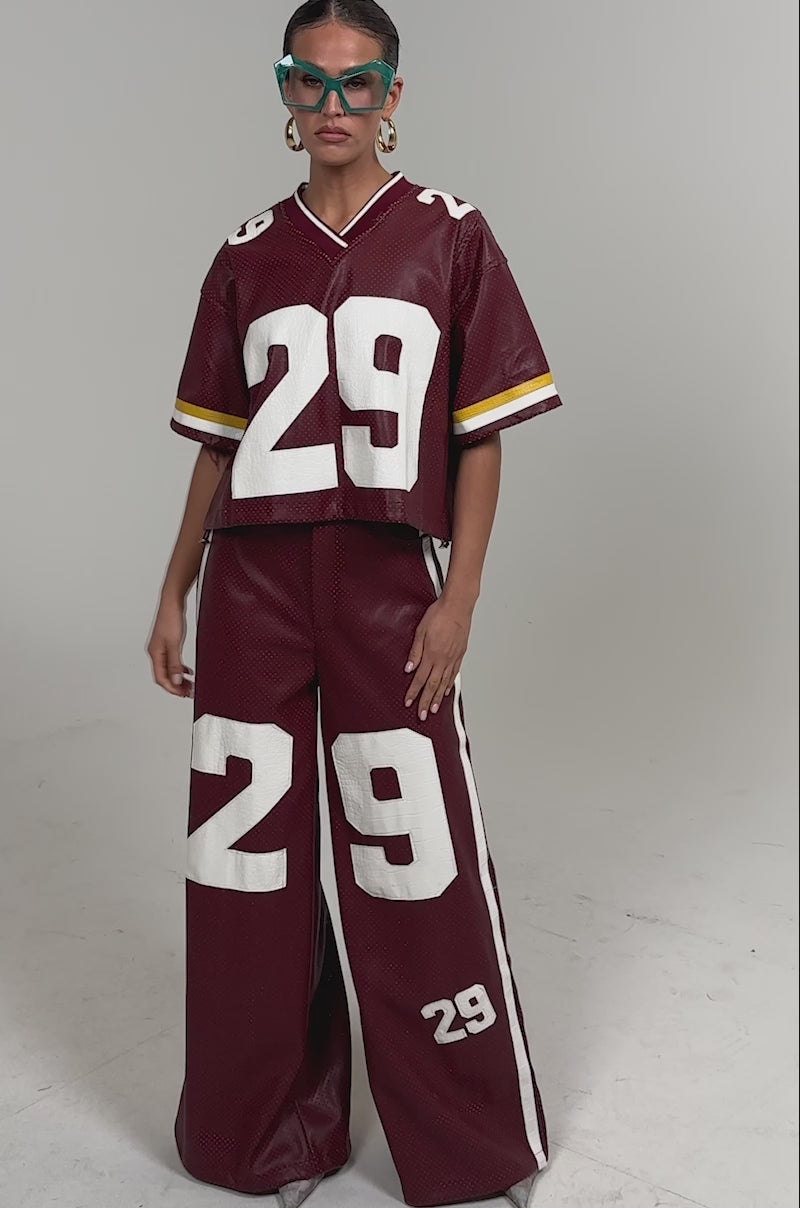 Video of woman modeling the LUCKY 29 TROUSER set—a sporty burgundy outfit with perforated detail, featuring the number 29 in white on both the cropped top and wide-leg pants.