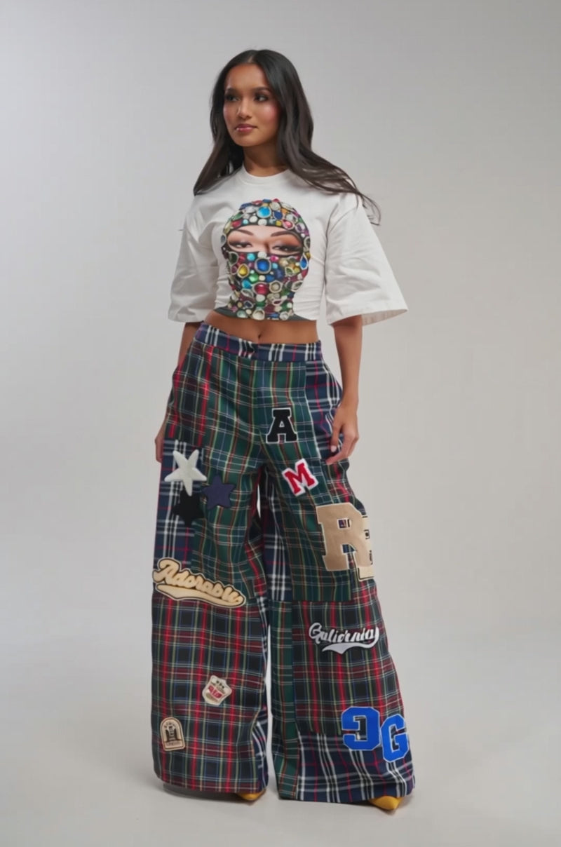 Video of woman modeling the ALL ABOUT ME PLAID TROUSER, featuring high-waisted, wide-leg plaid with bold colorful patches, stars, letters, and red, green, and blue checks against a plain background.