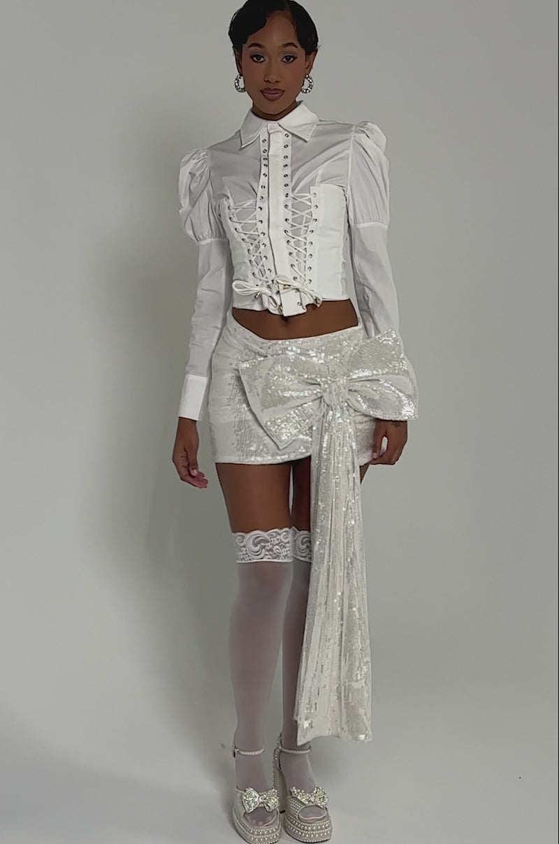 Video of woman modeling the SHINING DOWN ON YOU SEQUIN MINI SKIRT featuring a large bow. The background is neutral.