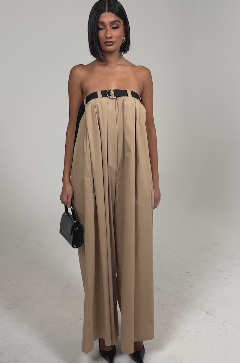 Video of woman modeling the DIANE STRAPLESS OVERSIZED KHAKI JUMPSUIT with a black belt, paired with a small black handbag and pointed black heels, set against a plain light background.