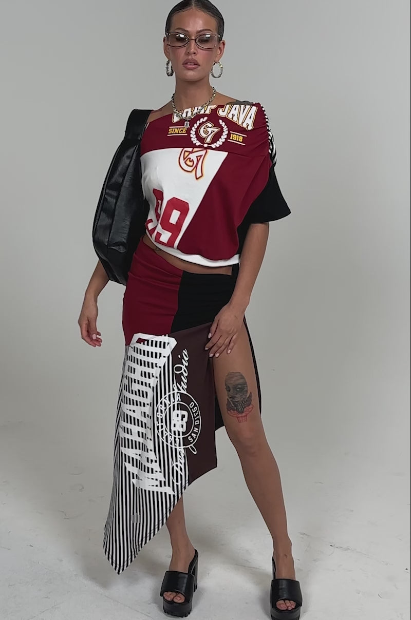 Video of woman modeling the SCHOOL SPIRIT REWORKED MIDI SKIRT with bold prints and sporty stripes, paired with black platform sandals and a black bag. Tattoos are visible on their thigh and torso.