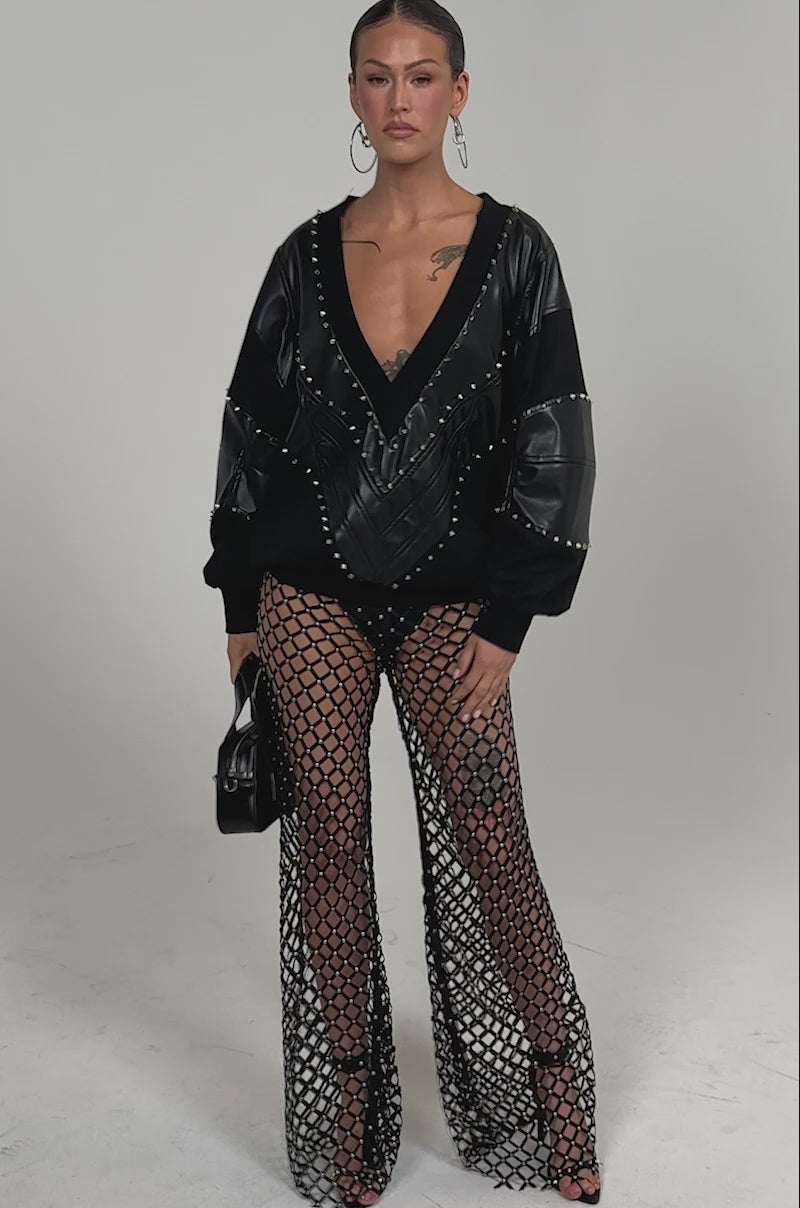 Video of woman modeling the LETS DO THIS FAUX LEATHER SWEATSHIRT, styled with black mesh fishnet pants, hoop earrings, and a black handbag with silver buckles, showcasing bold streetwear against a plain background.