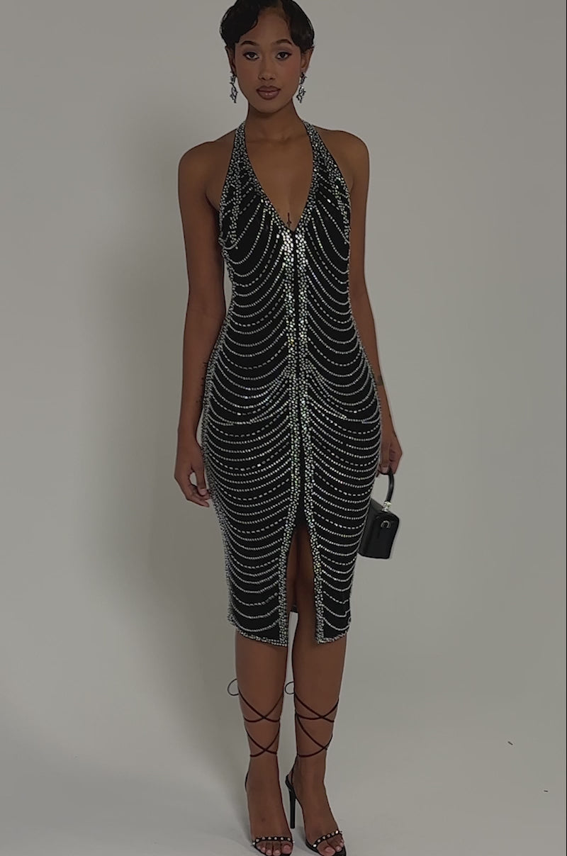 Video of woman modeling the LANA RHINESTONE MIDI DRESS, a black, form-fitting hourglass illusion dress adorned with sparkling swirling rhinestones. She holds a small black handbag, her short wavy hair completing the chic look.
