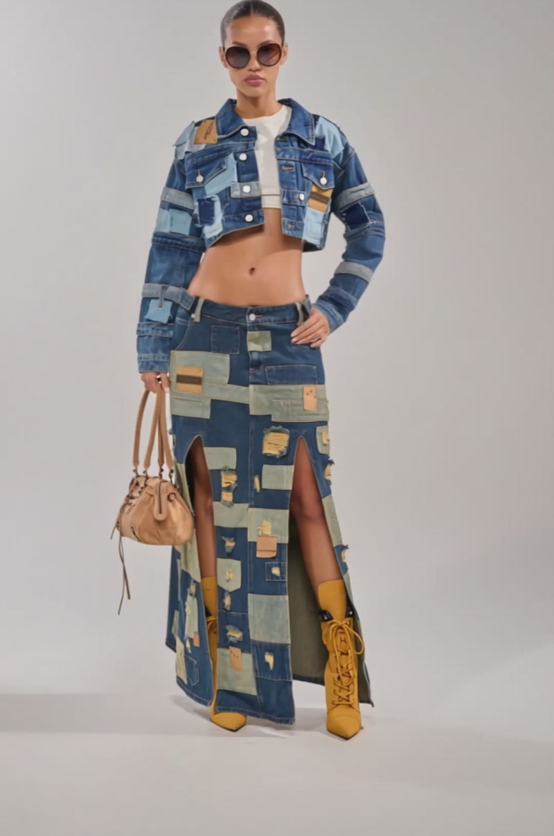 A video of a woman wearing the ACT UP PATCHWORK DENIM JACKET, matching maxi skirt with front slits, tan boots, oversized sunglasses, and carrying a tan handbag.